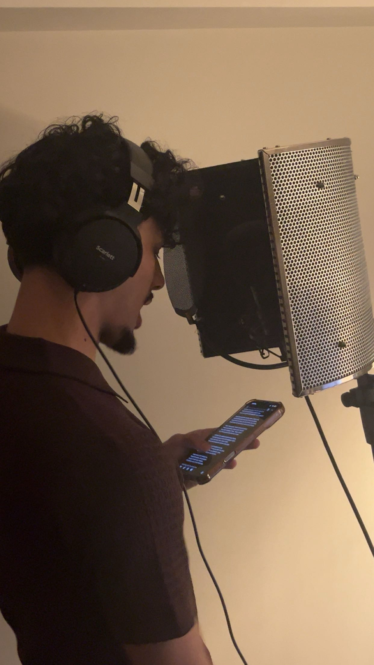 Artist recording a vocal with headphones, a reflection filter, and lyrics on a phone
